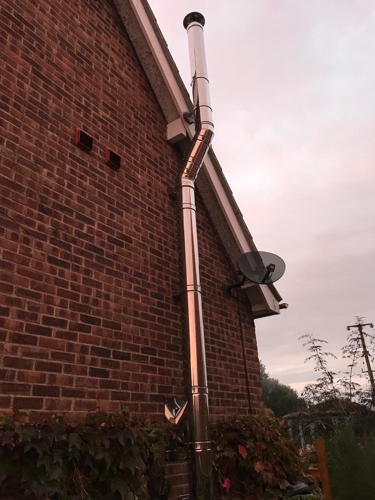 Stainless steel external flue on brick exterior — HETAS registered flue installation, Norfolk