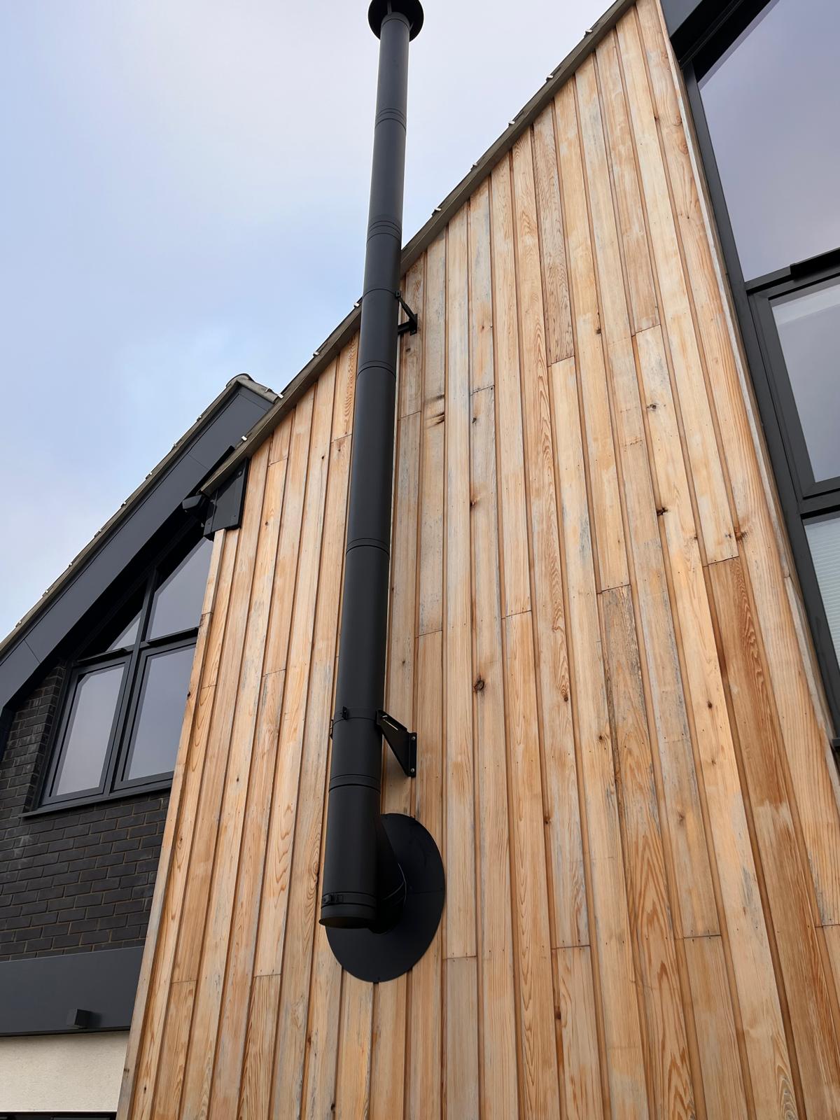 Cylinder wood burning stove installed on glass hearth in white room — Norwich