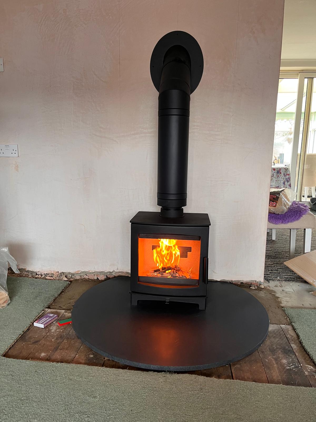 Wood burning stove installation on round slate hearth with fire burning — Watmore's Woodburners, Norfolk