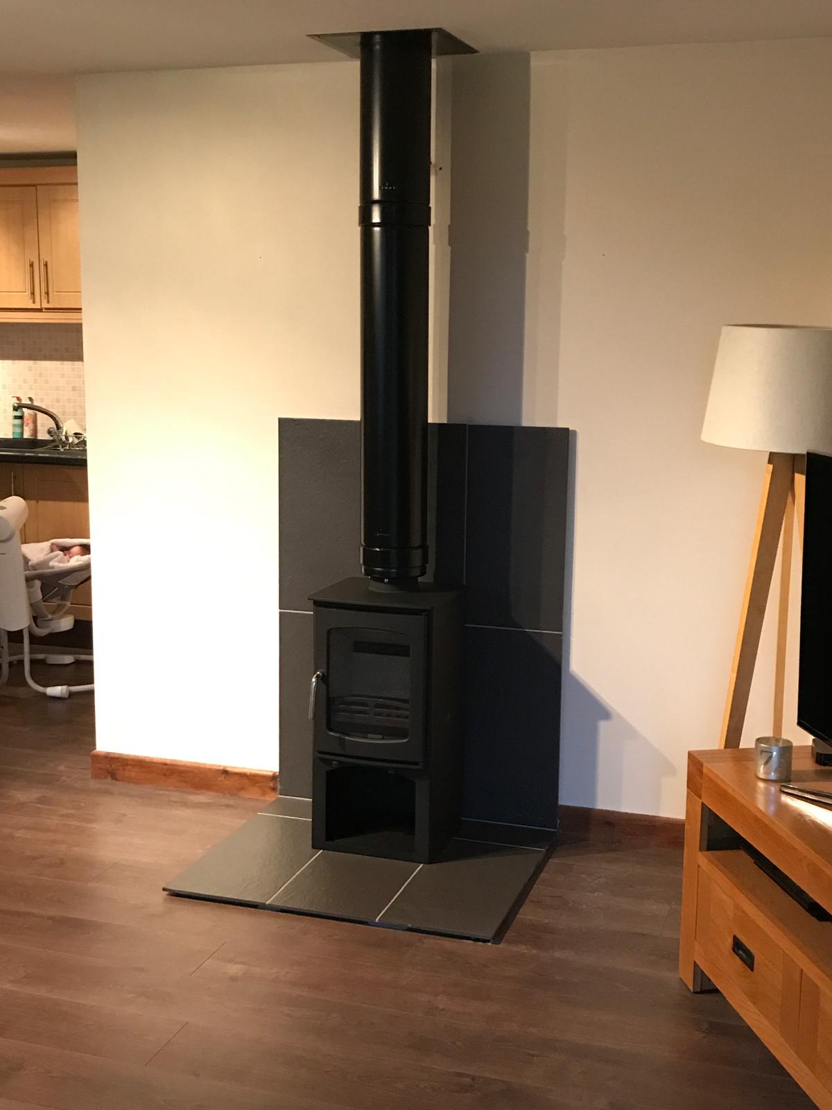 Wood burning stove with black slate back panel installed in living room — Norfolk