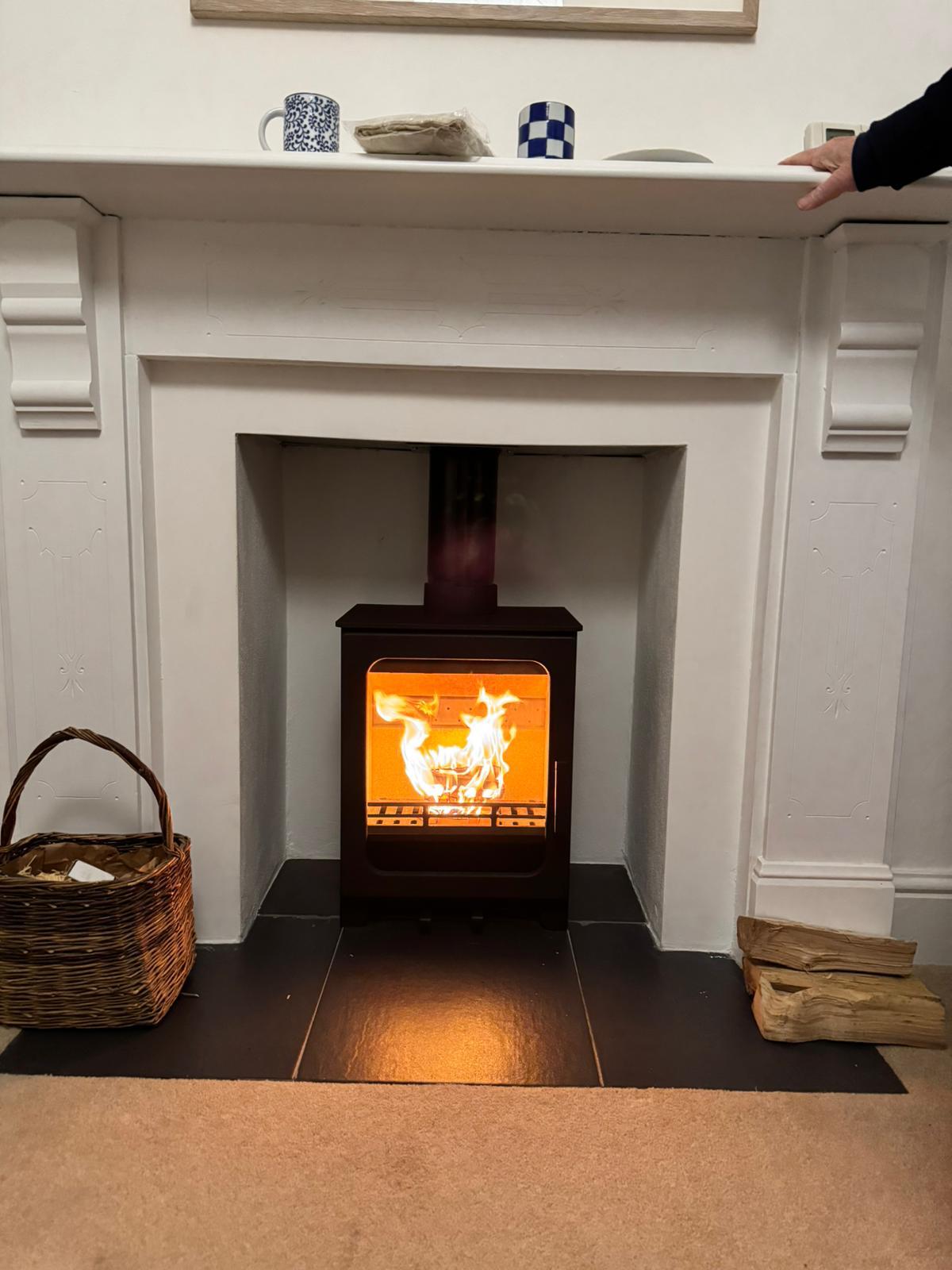 Completed woodburner installation with white fireplace surround, fire lit — Norwich, Norfolk